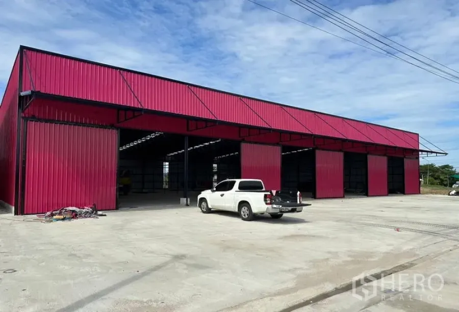Warehouse for rent in Ban Pho, Chachoengsao - Exterior perspective of the red metal warehouse blocks with spacious concrete yard for truck parking.