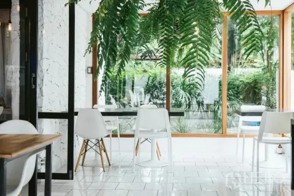 Retail Space for rent in Khlong Toei, Bangkok - Sunlit dining area with white chairs, wood‑trimmed full‑height windows and lush garden views.