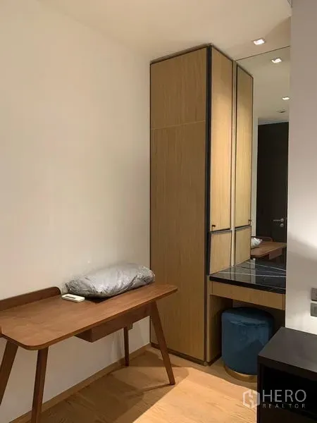 Condominium for rent in Khlong Toei, Bangkok - Work nook with wooden desk, tall built-in wardrobe, and mirrored vanity.