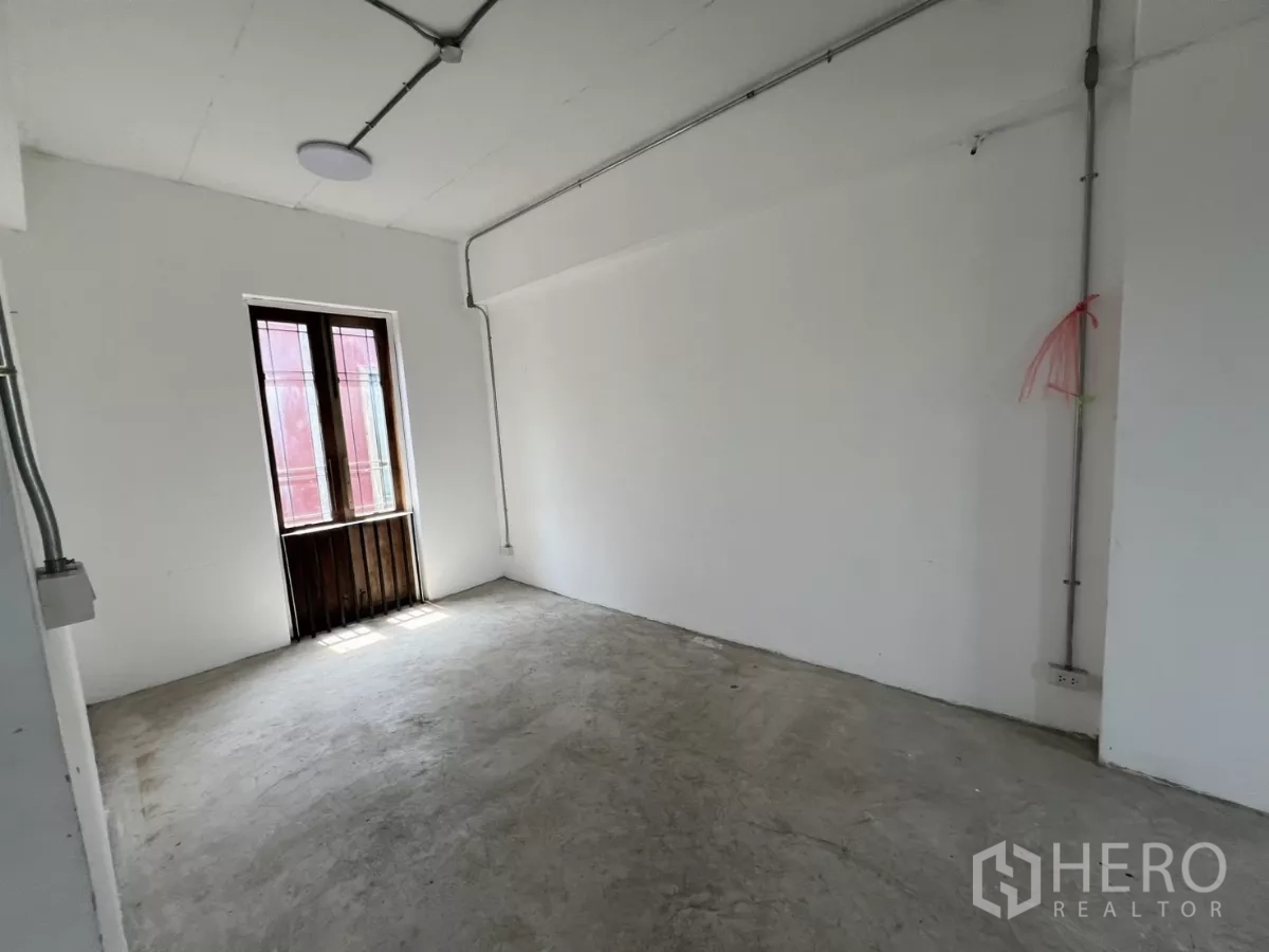 Retail Space for rent in Khlong Toei, Bangkok - Simple white room with a concrete floor and a small wooden-framed window.