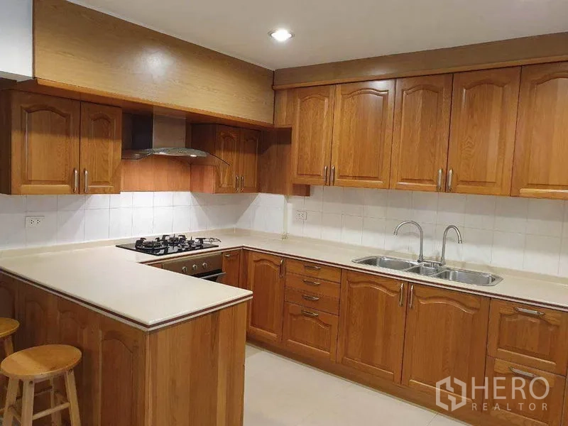 Detached House for rent in Phra Khanong, Bangkok - U-shaped kitchen with wooden cabinets, gas hob, range hood and double sink.