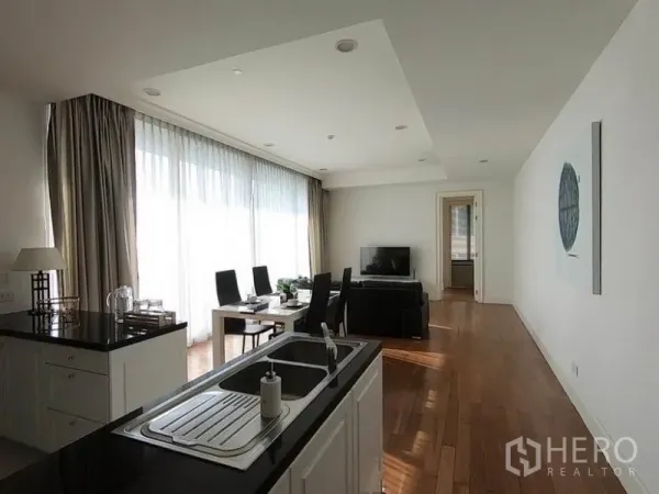 Condominium for rent in Watthana, Bangkok - Open kitchen with island and double sink overlooking dining and living areas with large windows.