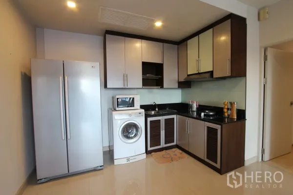 Condominium for rent or sale in Watthana, Bangkok - Modern L-shaped condo kitchen with large fridge, microwave, in-unit washing machine, ample cabinets and black stone countertop.
