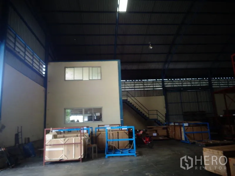 货栈 出租或出售在Lat Lum Kaeo, Pathum Thani - 高拱钢结构屋顶下的仓库内景，带两层办公室盒体与楼梯、木箱。