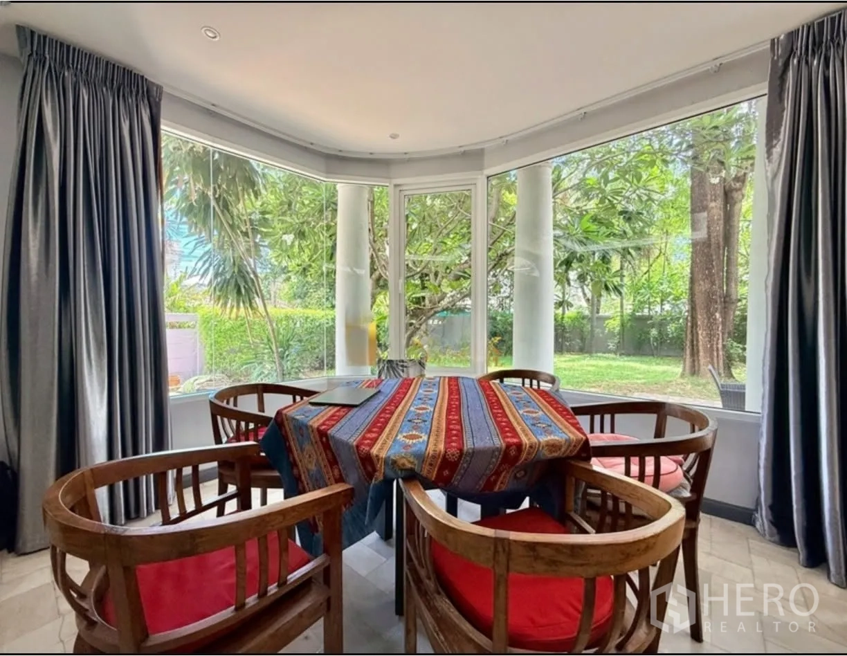 Detached House for rent in Phra Khanong, Bangkok - Dining area with wooden chairs and bay windows overlooking greenery.