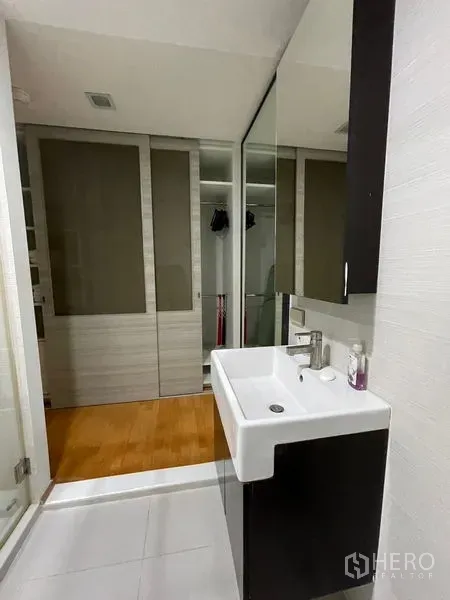 Condominium for sale in Khlong Toei, Bangkok - Vanity area with large mirror and sliding wardrobe doors next to the bathroom.