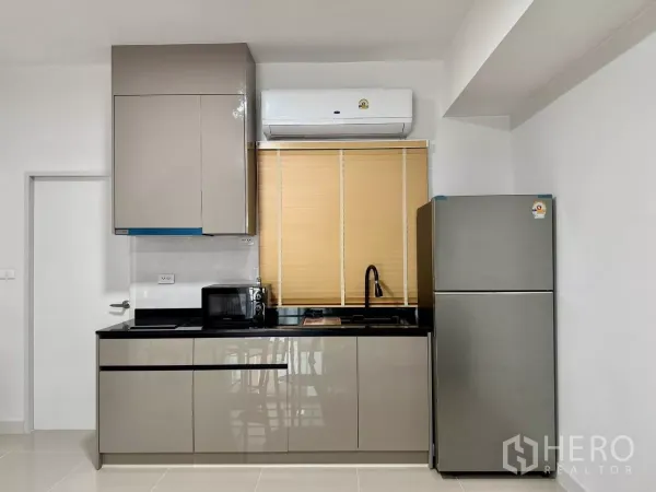 Townhouse for rent in Bang Phli, Samut Prakan - Compact modern kitchen with glossy cabinets, black countertop, sink, microwave and fridge
