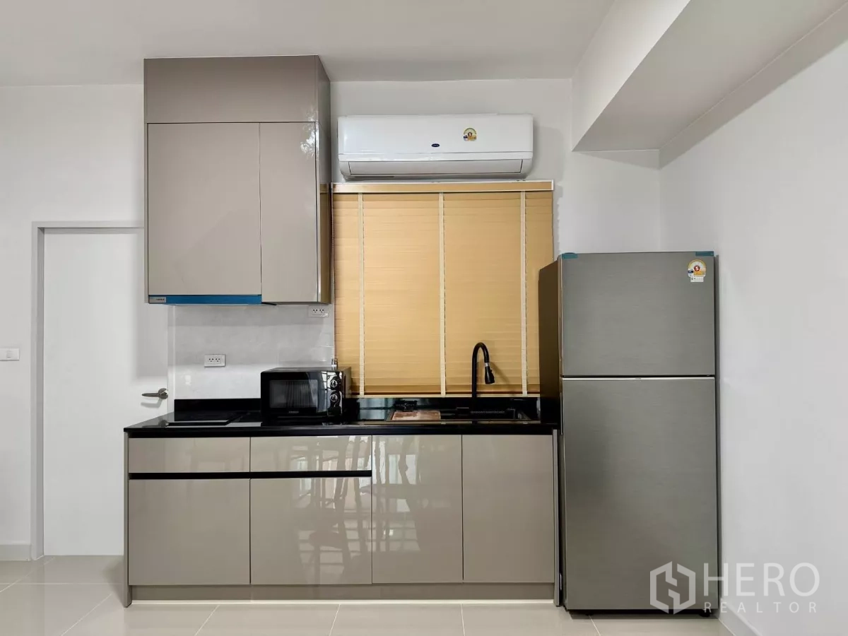 Townhouse for rent in Bang Phli, Samut Prakan - Compact modern kitchen with glossy cabinets, black countertop, sink, microwave and fridge