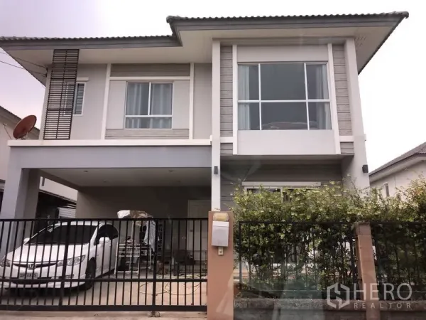独立式住宅 出售在Saphan Sung, Bangkok - 现代两层独栋别墅外观，大片窗户、带顶双车位车棚、黑色金属围栏与绿篱