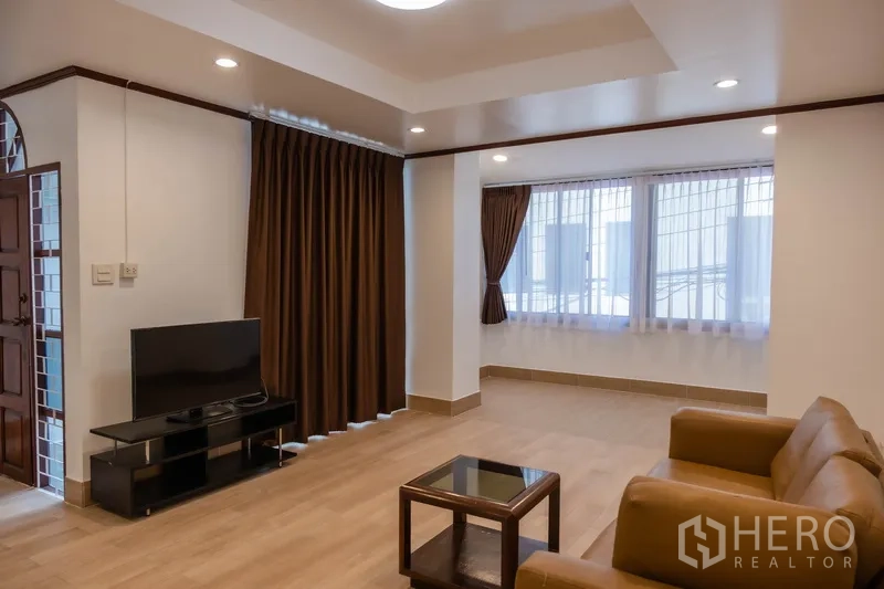 Home Office for rent in Khlong Toei, Bangkok - Spacious living room with sofa, TV unit and large curtained windows.
