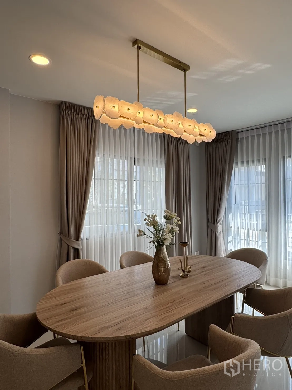 บ้าน for rent in Bang Phli, Samut Prakan - มุมรับประทานอาหาร เก้าอี้บุผ้า 6 ที่รายล้อมโต๊ะไม้ ภายใต้แสงโคมแขวนโทนอุ่น