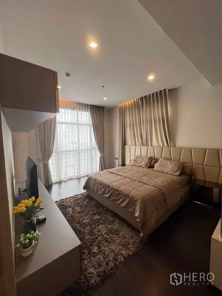Condominium for rent or sale in Watthana, Bangkok - Sunlit bedroom with king bed, TV console and floor-to-ceiling drapes opening to city views.