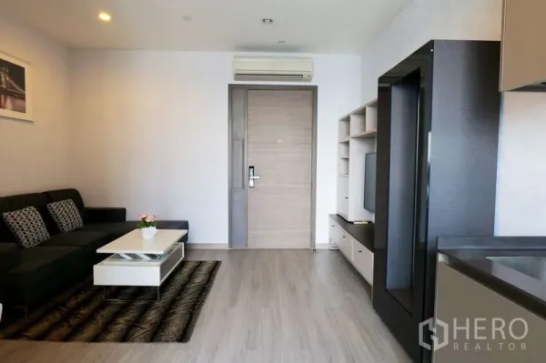 Condominium for rent in Watthana, Bangkok - Open-plan living area viewed from the kitchen with sofa, media wall and main entrance door.