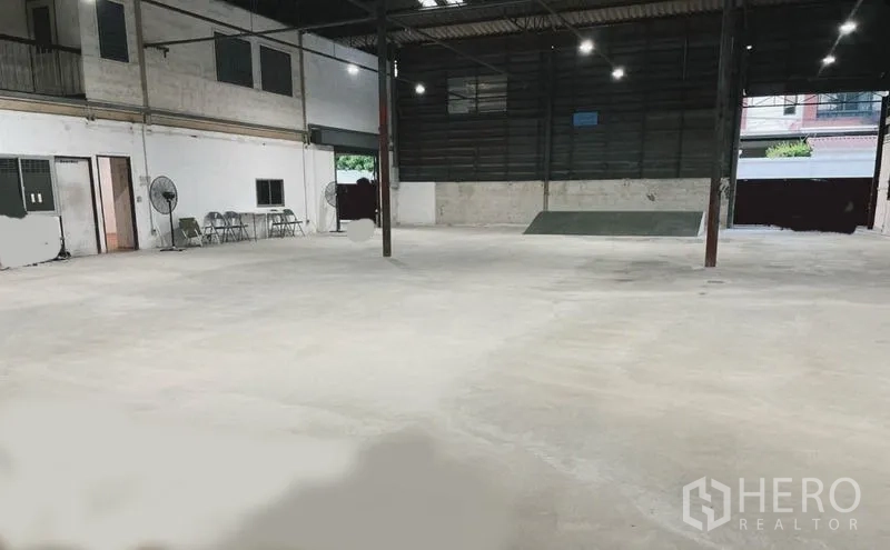 Warehouse for rent or sale in Mueang Nonthaburi, Nonthaburi - Open warehouse floor with a loading ramp, wide entry gate, and wall-mounted fans for ventilation.