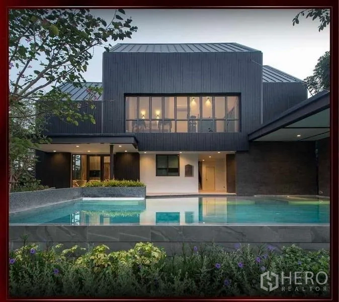 Detached House for sale in Khan Na Yao, Bangkok - Estate clubhouse with large outdoor swimming pool and landscaped deck at dusk.