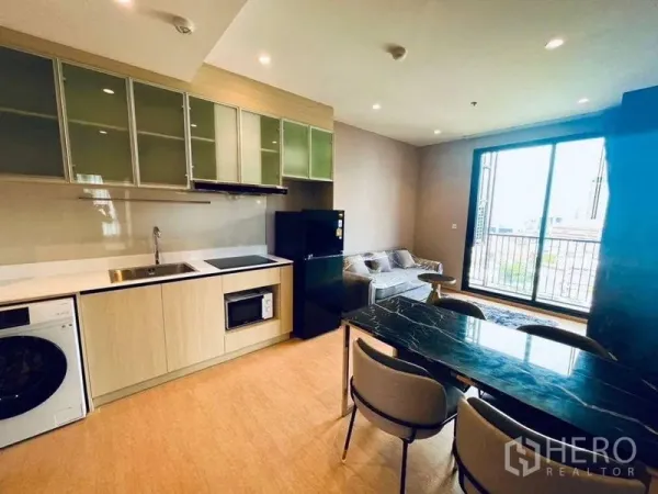Condominium for rent or sale in Watthana, Bangkok - Dining area with black marble table next to kitchen and sliding doors to balcony