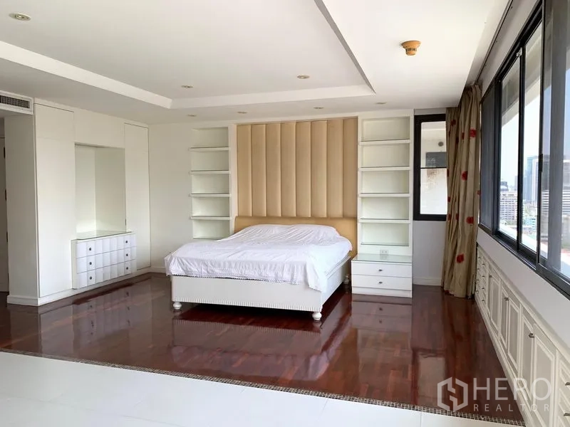 Condominium for sale in Khlong Toei, Bangkok - Spacious master bedroom with padded headboard, white built-ins and city views.