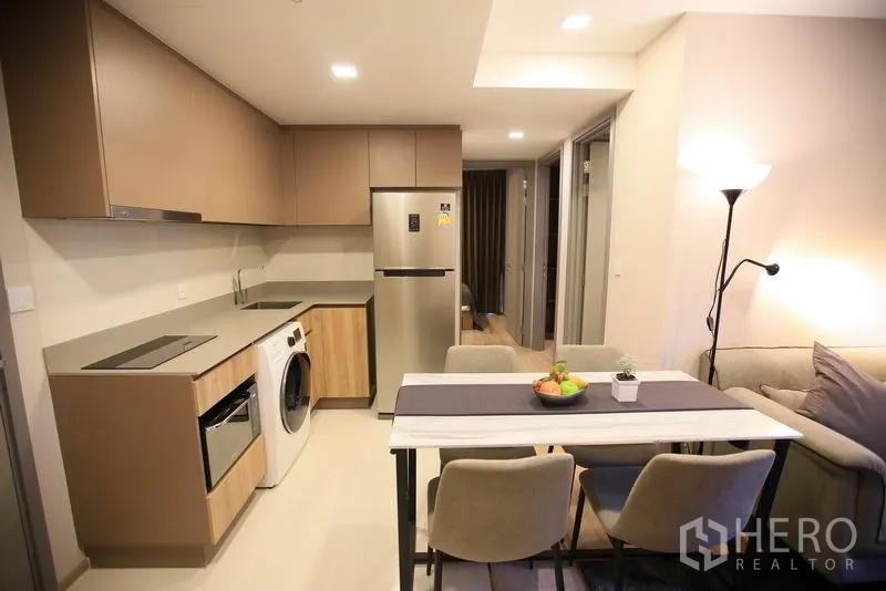 公寓 出租或出售在Watthana, Bangkok - 明亮小厨房与餐桌，浅色橱柜与筒灯照明。