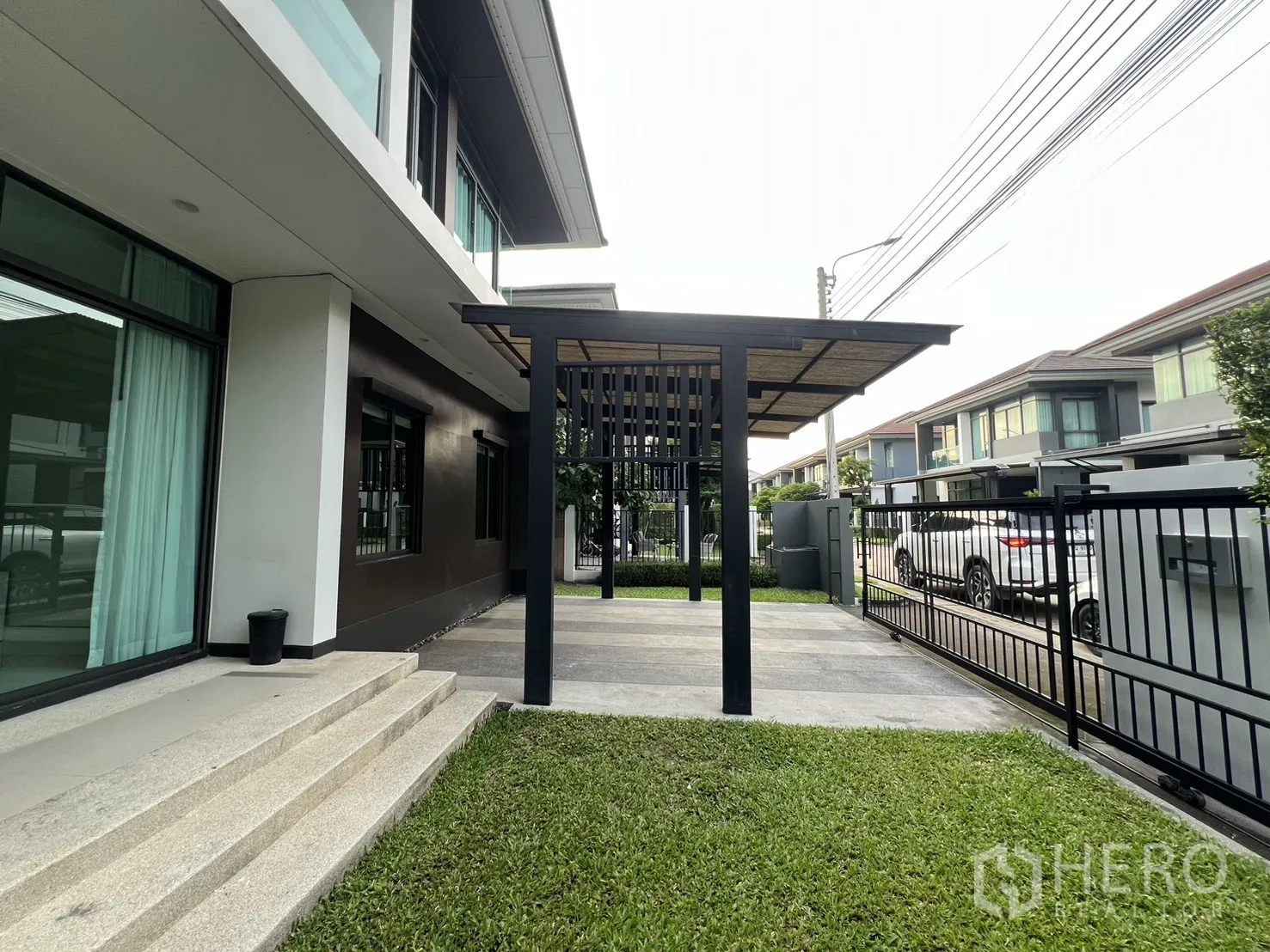 Detached House for rent in Bang Kapi, Bangkok - Front yard with grass, steps to sliding glass doors and a steel canopy.