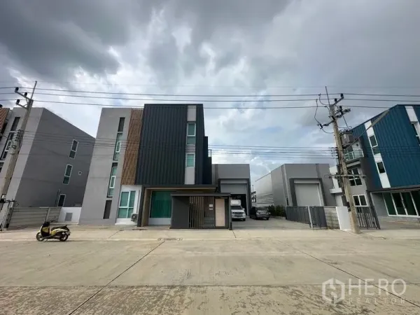Warehouse for sale in Pathum Thani - Modern three-storey office facade with attached warehouse and gated parking on a wide road in Lam Luk Ka, Pathum Thani.