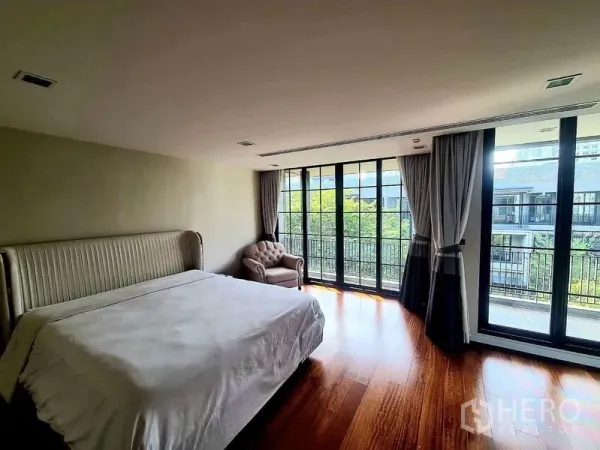 联排别墅 出租在Watthana, Bangkok - 宽敞主卧，落地窗通向阳台，木地板与浅色床具