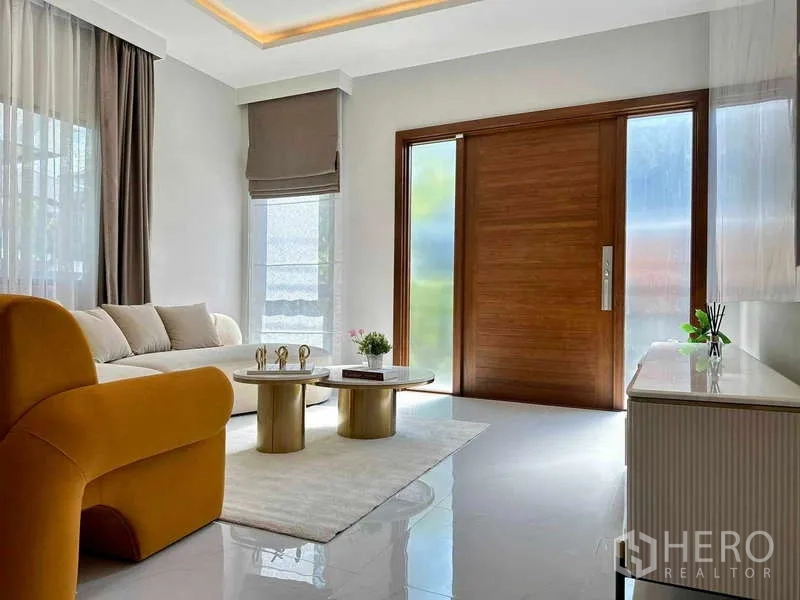 Detached House for rent or sale in Bang Phli, Samut Prakan - Light-filled living room with large wooden entrance door, sofa and twin marble-top tables.