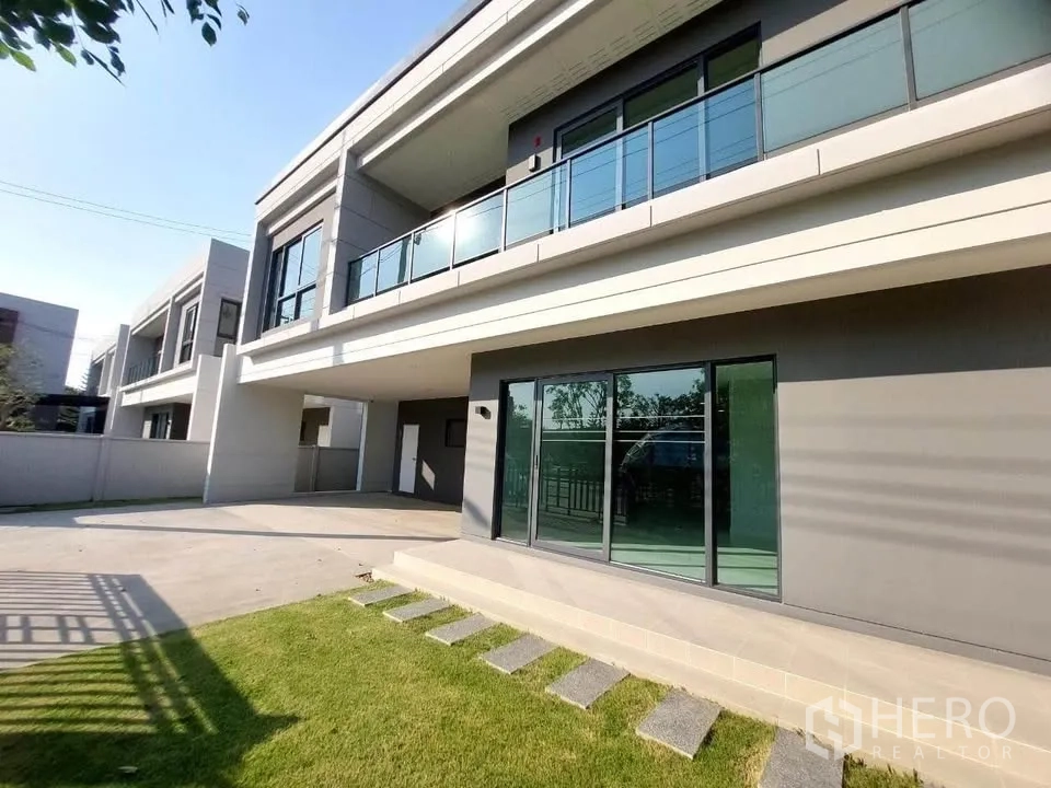 Detached House for rent or sale in Bang Phli, Samut Prakan - Lawn and patio beside the house with sliding doors and a glass balcony above.