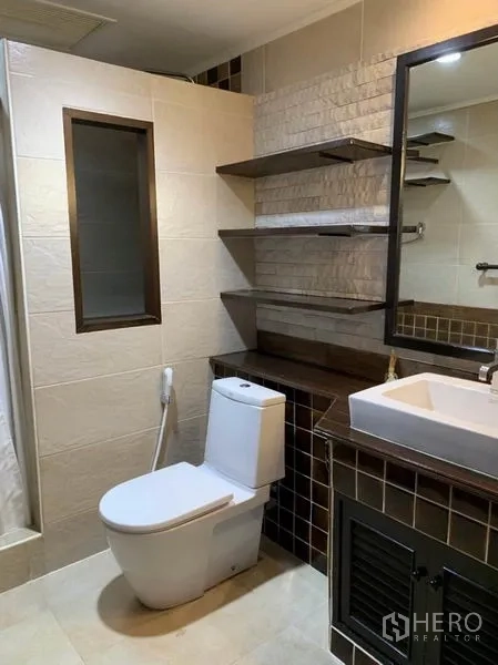 Townhouse for rent in Khlong Toei, Bangkok - Modern bathroom with vanity, wall shelves, mirror and a toilet in neutral tiles.