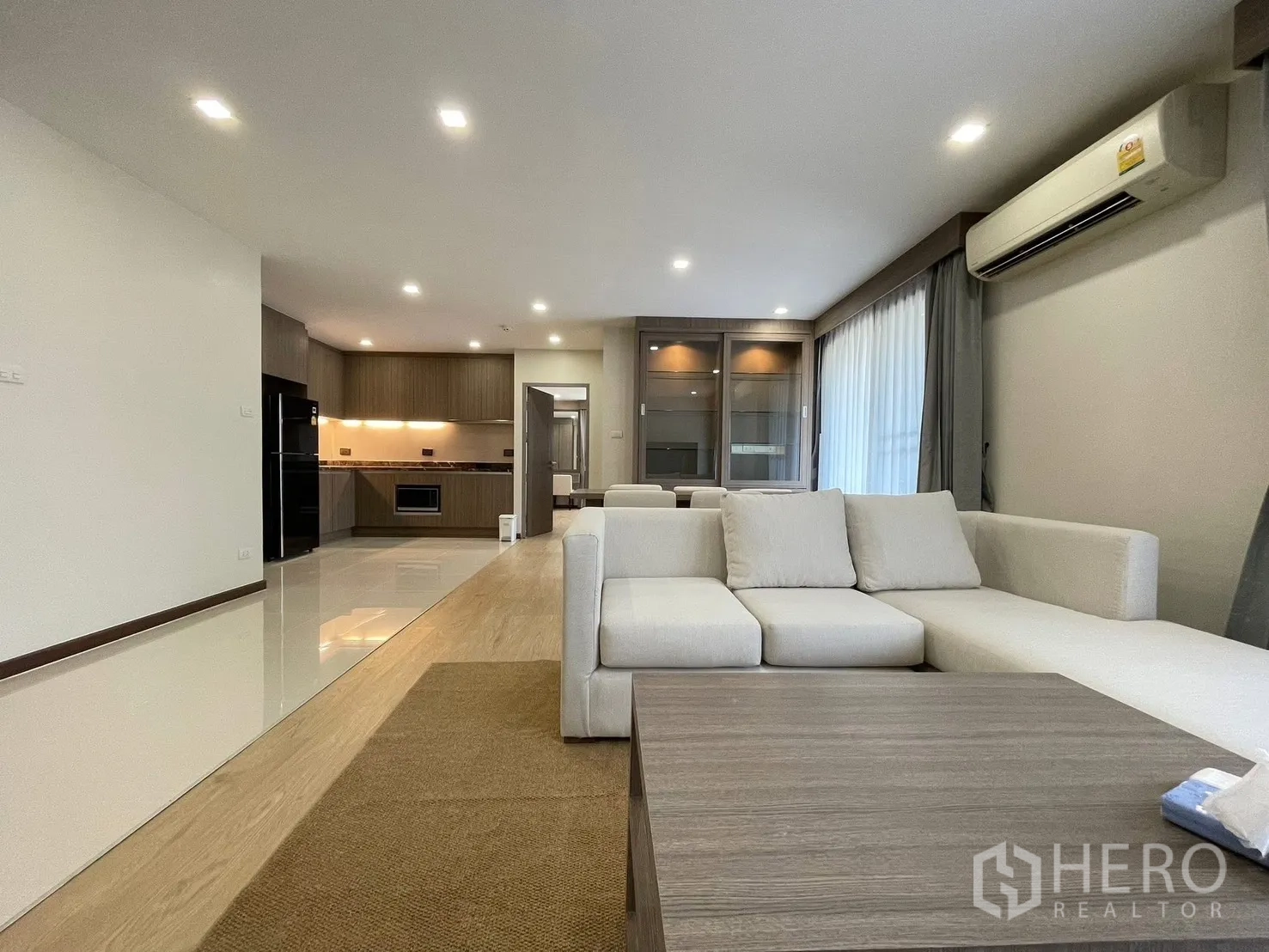 公寓 for rent in Watthana, Bangkok - 从沙发望向木质橱柜厨房与内置收纳，地面为亮面瓷砖。