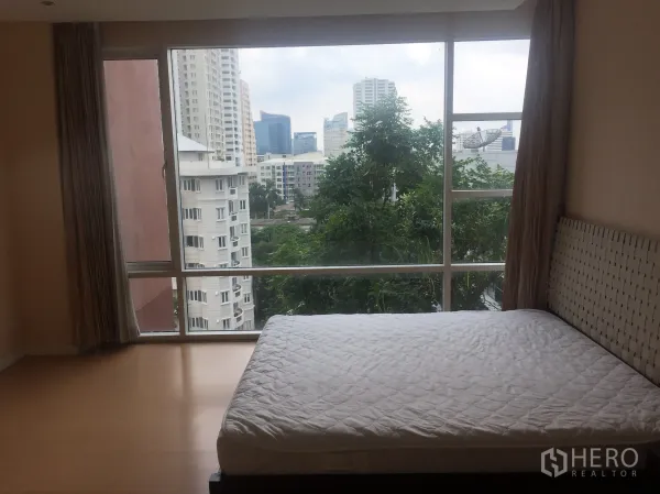 Condominium for rent or sale in Watthana, Bangkok - Master bedroom with large picture windows overlooking greenery and city skyline near BTS Ekkamai.