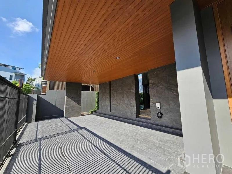 Detached House for rent in Wang Thonglang, Bangkok - Covered carport with wood ceiling and stone driveway beside a secure metal fence.