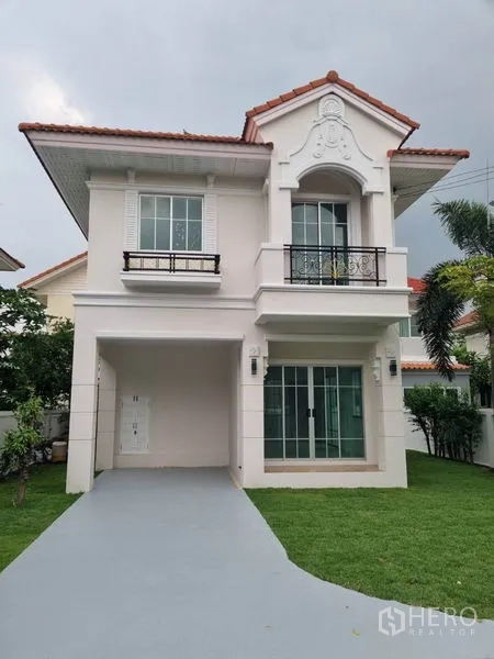 บ้าน ขายในNonthaburi - บ้านเดี่ยวสองชั้นหลังคากระเบื้องสีแดง มีที่จอดรถและสนามหญ้าหน้าบ้าน.