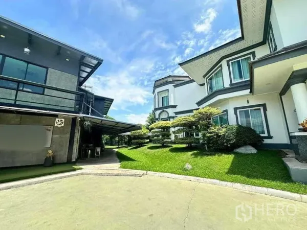Detached House for sale in Khlong Luang, Pathum Thani - Landscaped courtyard with trimmed trees between the main white house and a modern glass-sided pavilion.
