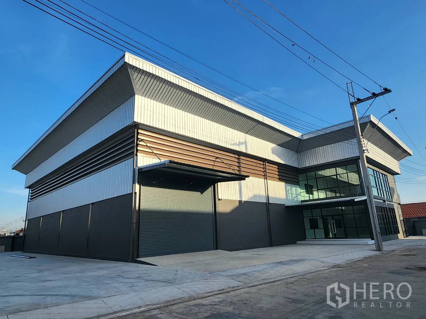 Factory for rent or sale in Bang Sao Thong, Samut Prakan - Modern factory exterior with large roller shutter, covered loading bay, and glass-front two-storey office.