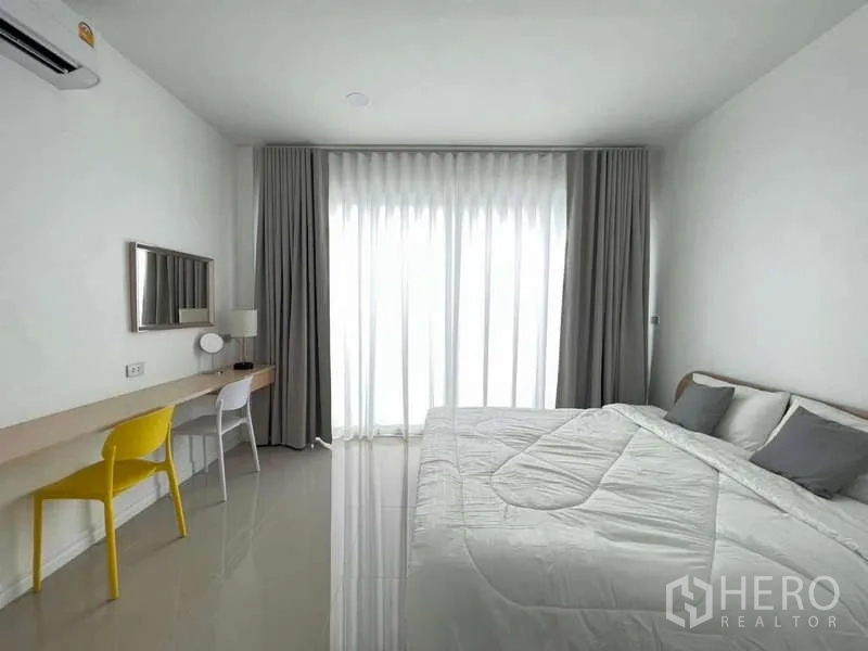 Detached House for rent in Lat Krabang, Bangkok - Bedroom with king bed, long study desk and sheer curtains filtering natural light.