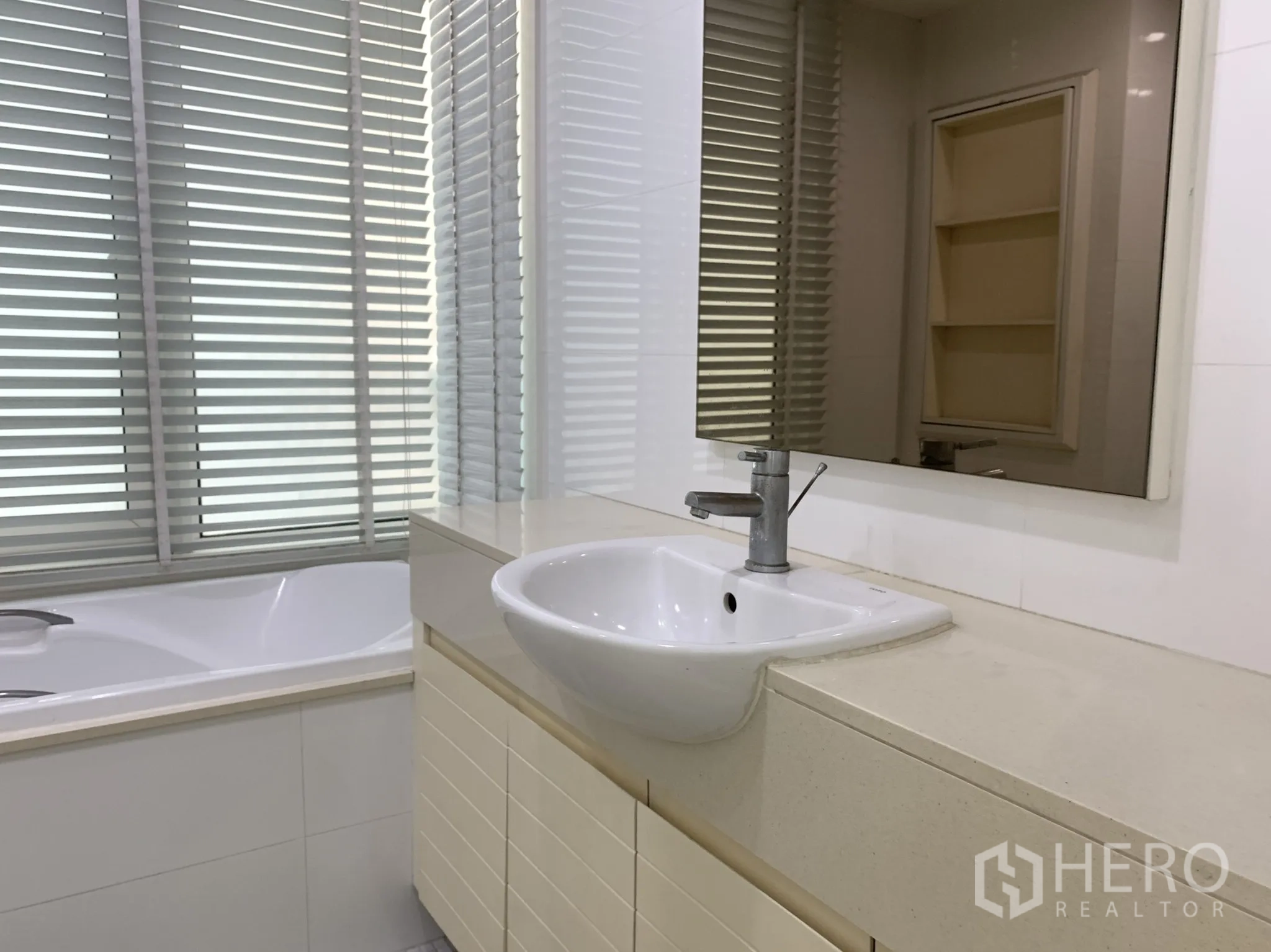 Condominium for rent in Khlong Toei, Bangkok - Bathroom with long vanity, basin sink and bathtub beside louvered privacy windows.