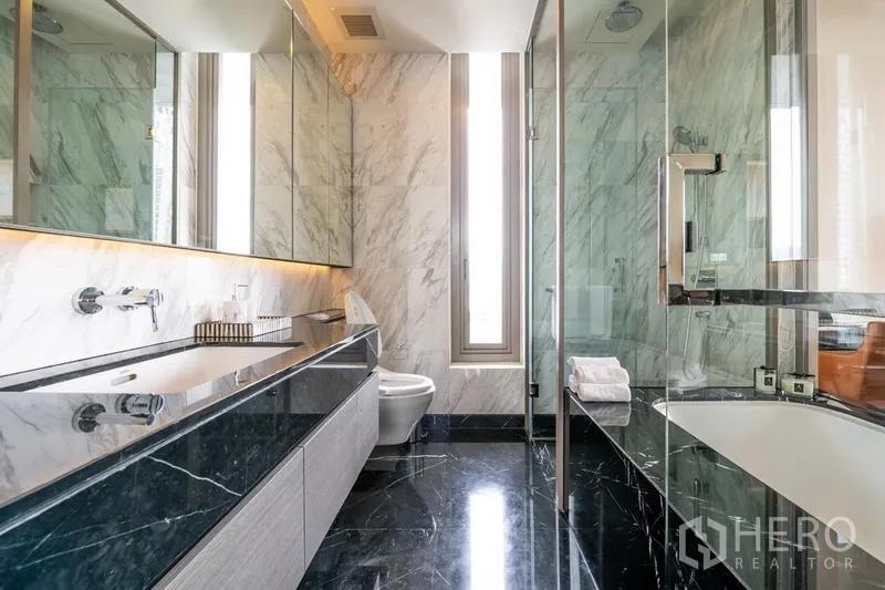 Condominium for rent or sale in Bang Rak, Bangkok - Luxury bathroom featuring long stone vanity, toilet, glass shower and bathtub with marble finishes.