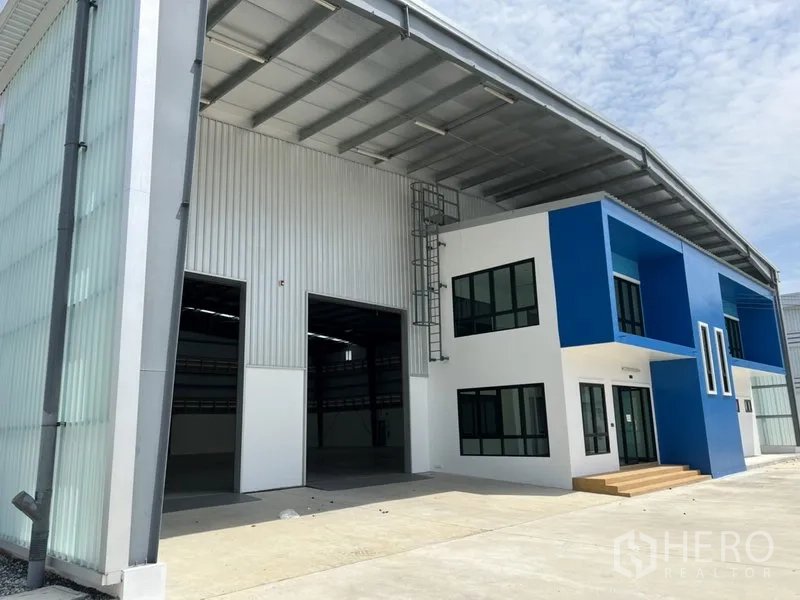 Factory for rent in Bang Sao Thong, Samut Prakan - Modern factory exterior with blue-and-white office block, covered loading area and large roller door.