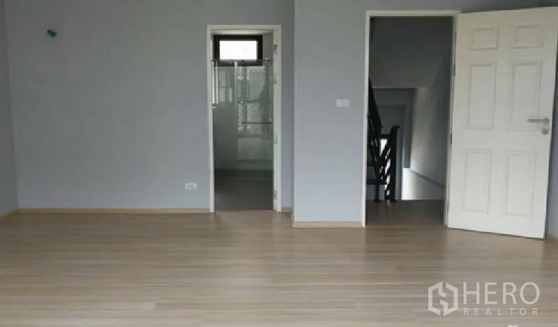 Townhouse for rent in Yan Nawa, Bangkok - Spacious unfurnished bedroom with laminate flooring and doors leading to the bathroom and stairwell.