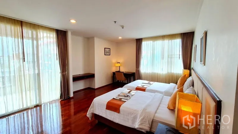 Apartment for rent in Khlong Toei, Bangkok - Twin bedroom from another angle showing windows, bedside lamps and a study desk.