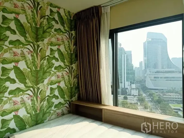 公寓 出租在Pathum Wan, Bangkok - 卧室一角，热带叶纹特色墙，大窗户眺望曼谷天际线。