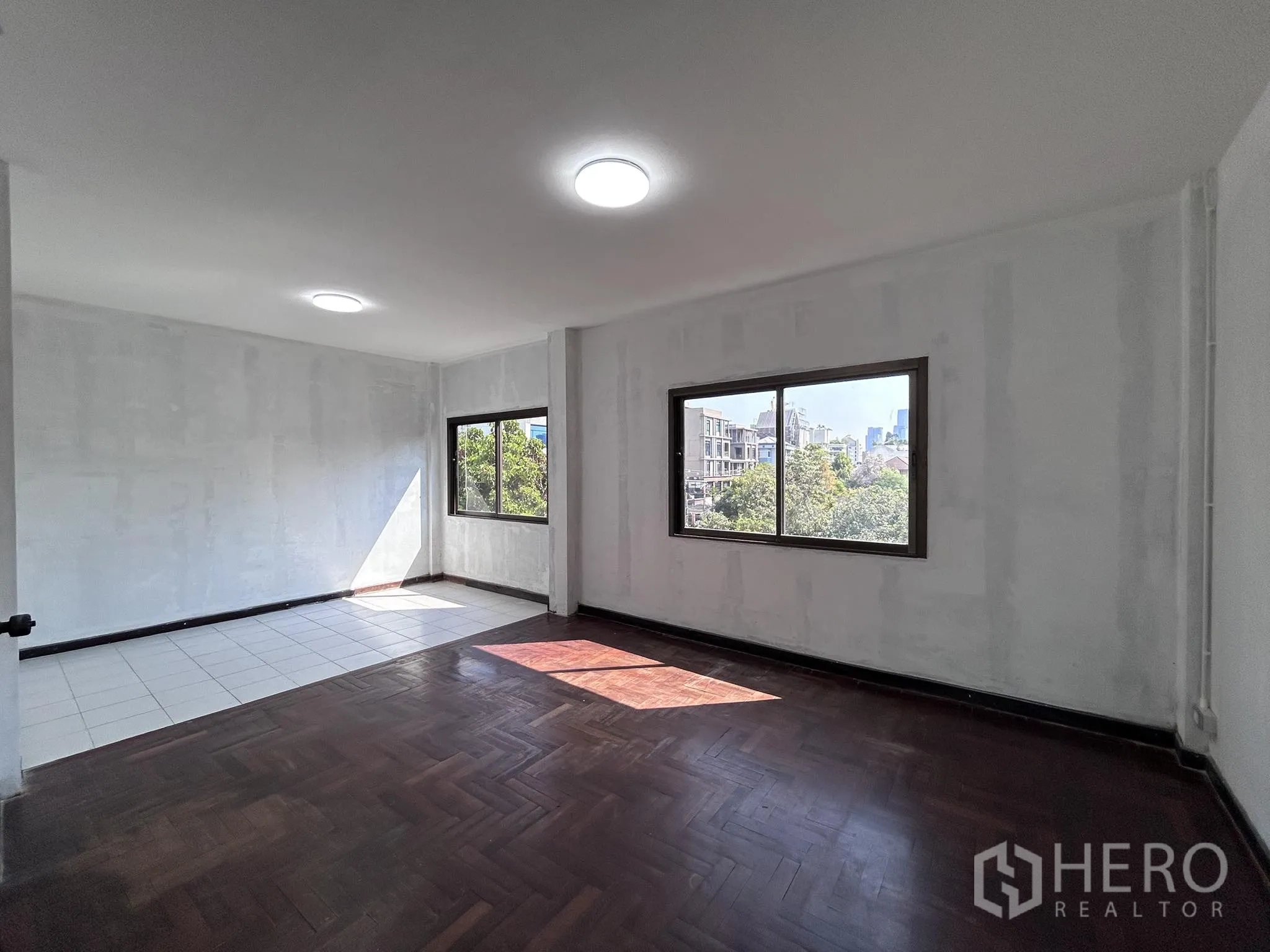 家庭办公室 for rent or sale in Watthana, Bangkok - 转角空间，瓷砖与木地板混搭，窗外城市景观。