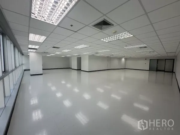 办公空间 出租在Watthana, Bangkok - 宽敞开放办公区，沿窗带设计，吊顶荧光灯，尽头为双扇玻璃门入口。