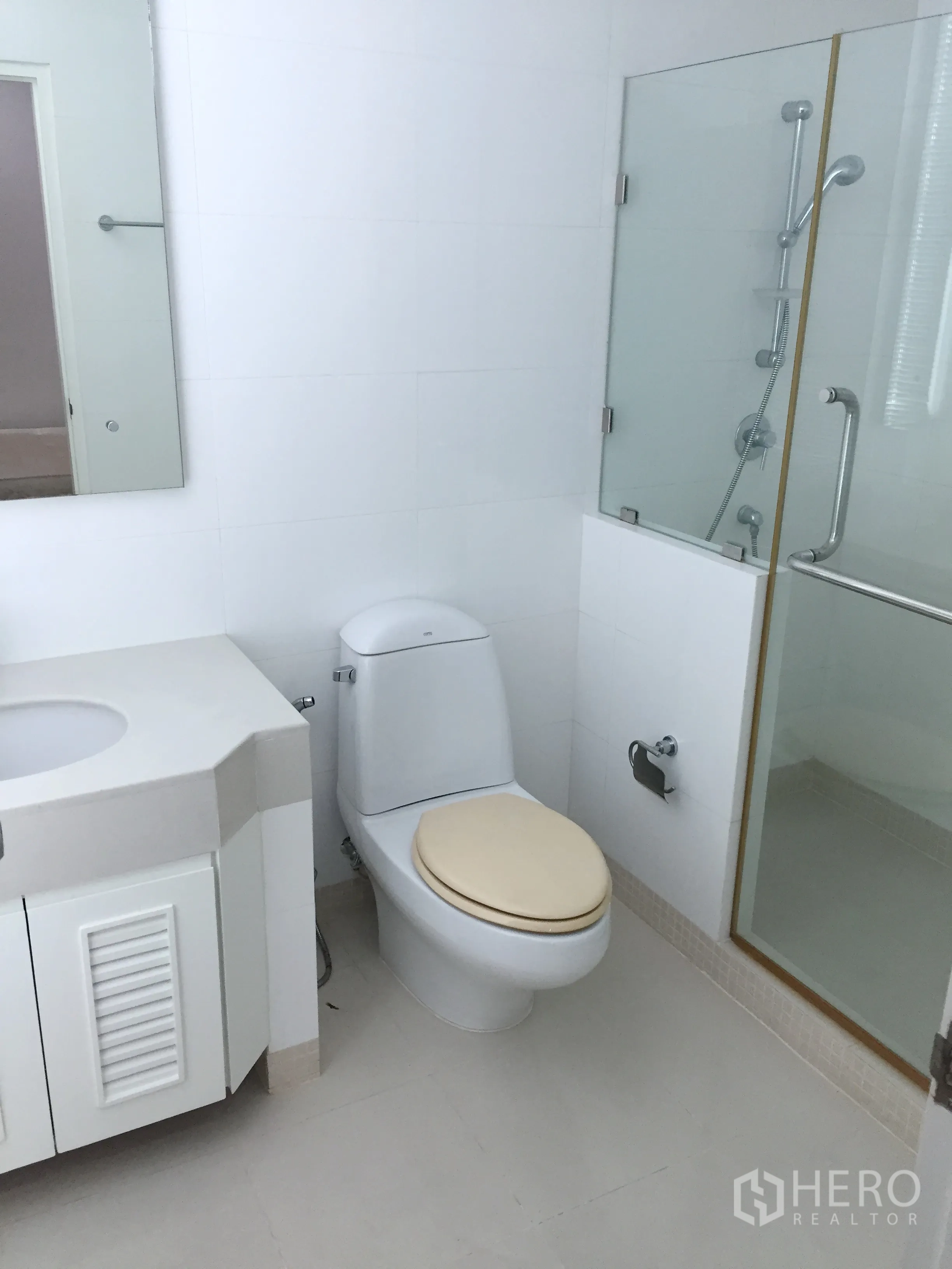 Condominium for rent in Khlong Toei, Bangkok - Clean white bathroom with toilet, sink cabinet, and a glass shower enclosure.