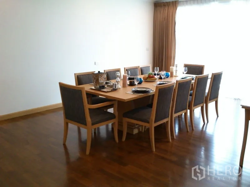Condominium for rent in Khlong Toei, Bangkok - Formal dining room with a 10-seat wooden table and place settings by a window.