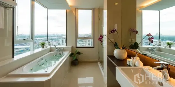 Apartment for rent in Khlong Toei, Bangkok - Spacious bathroom with long soaking tub, vanity and orchids beside floor-to-ceiling windows.