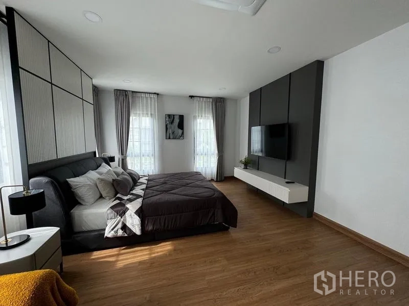 Detached House for rent or sale in Bang Phli, Samut Prakan - Master suite with TV feature wall opposite the king bed and tall curtained windows.