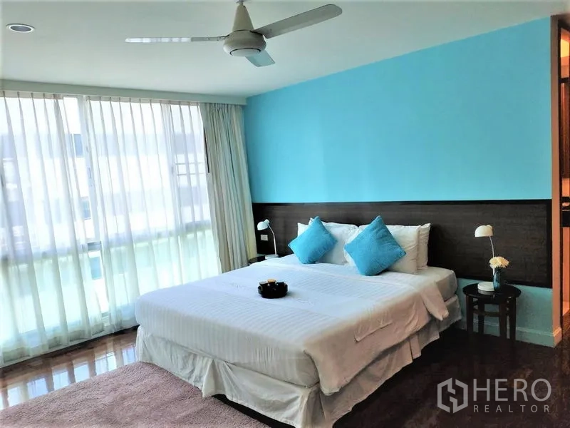 公寓 出租在Bang Rak, Bangkok - 明亮主卧，蓝色强调墙、特大床、落地窗纱帘与吊扇，位于是隆公寓。