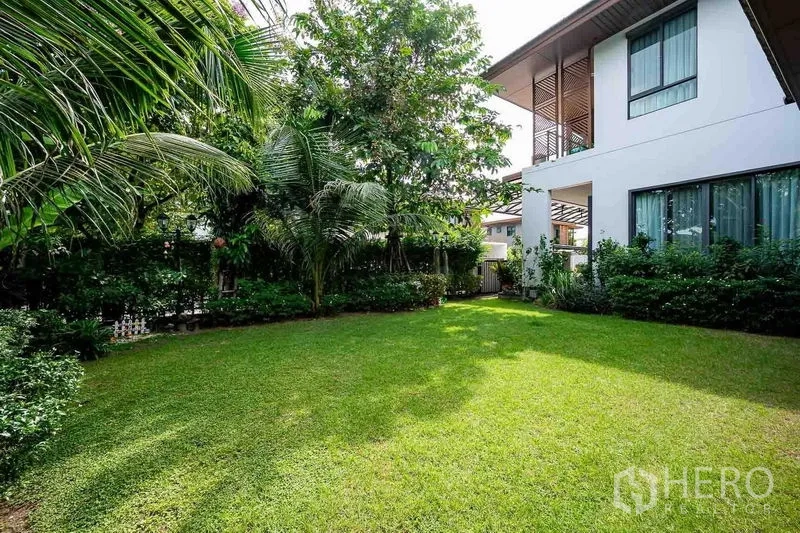 独立式住宅 出售在Prawet, Bangkok - 绿意草坪与白色两层住宅外观，周围环绕棕榈与灌木。