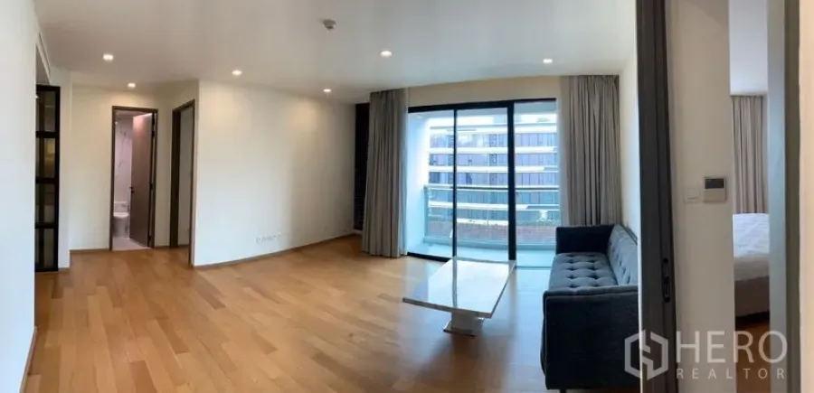 公寓 出售在Khlong Toei, Bangkok - 采光充足的客厅，木地板、沙发与茶几，推拉门通向观景阳台。